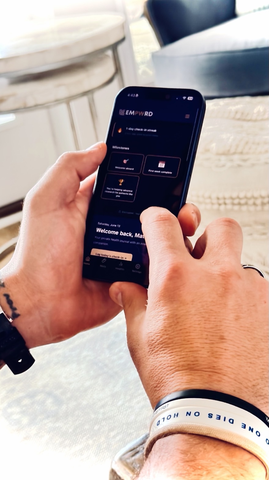 EMPWRD founder Matt Toresco using the EMPWRD Patient app on his iPhone, logging today's check-in from a sunlit living room.